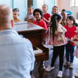 Image of children gathered around a piano for choir